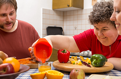 An older woman pouring squeezed juice in a cup with a man looking on at a kitchen table.